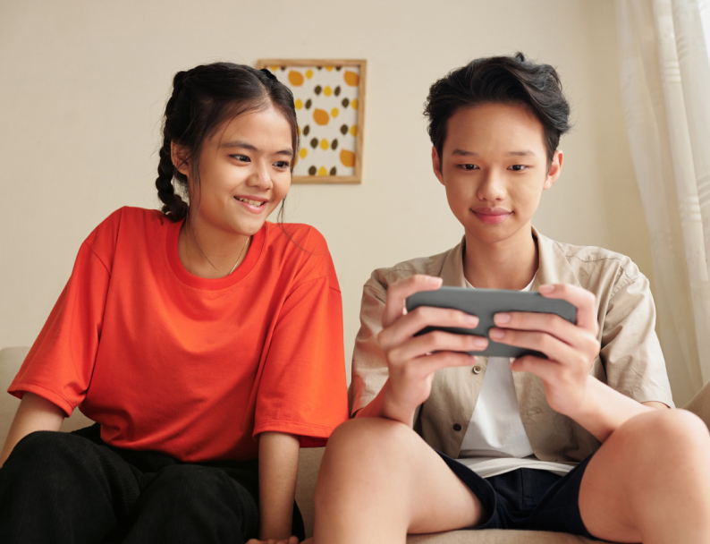 ソファに座ってスマートフォンを楽しそうに見ている兄妹